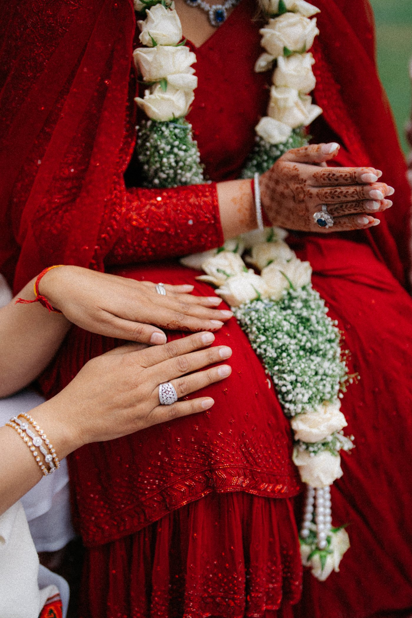 Hands resting on a red saree, with white rose and gypsophila garlands
